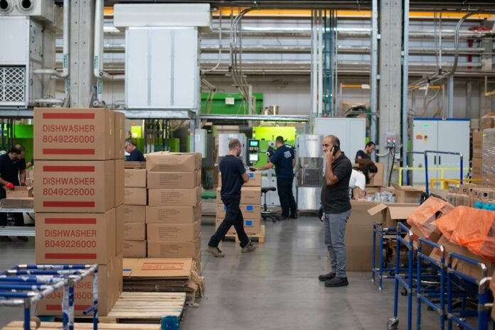 A group of workers in a factory surrounded by stacked boxes, engaged in organizing what a request for proposal does and managing inventory.